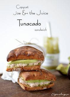 two sandwiches sitting on top of a wooden cutting board next to an avocado