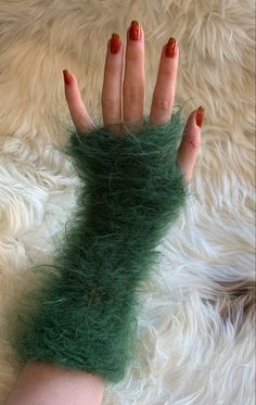 a woman's hand with red nails and green fake fur on top of it