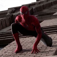 the amazing spider - man is sitting on top of a brick building with his legs spread out