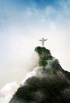 the statue is standing on top of a mountain with fog in the air around it