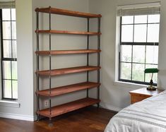 a room with a bed, window and shelves on the wall in front of it