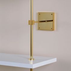 a white shelf with a gold door handle on it and a square light fixture hanging from the wall