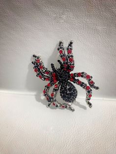 a red and black spider brooch sitting on top of a white surface with its eyes closed