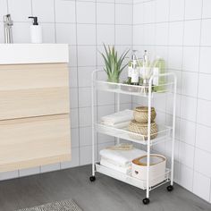 a bathroom with white tile walls and flooring next to a shelf filled with towels