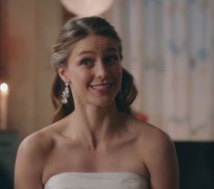 a woman in a white strapless dress smiles at the camera with candles behind her