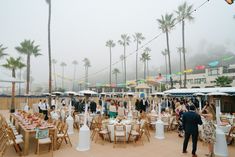 a group of people standing around tables with umbrellas over them and palm trees in the background