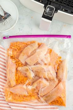 some chicken is in a plastic bag on the counter next to a plate and fork