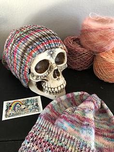 a skull wearing a knitted hat next to balls of yarn and a sticker