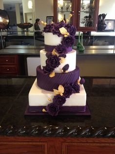 a three tiered cake with purple flowers on the top and bottom, sitting on a counter