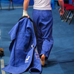 a man in blue pants and white shirt carrying a large bag on his back while walking across a tennis court