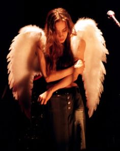 a woman with angel wings standing in front of a microphone and holding her arms crossed