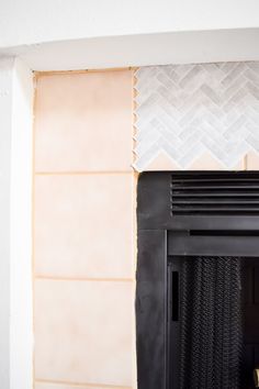 a fire place in the corner of a room with white tiles on the wall and a black fireplace