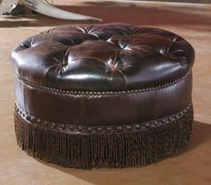 a brown leather ottoman with tassels and fringe trimming on the bottom half