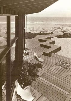 an outdoor deck overlooking the ocean with chairs and potted plants in front of it