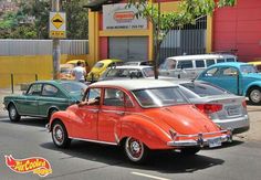 an orange and white car driving down a street next to other cars in front of a building