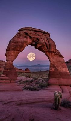 the full moon is seen through an arch shaped rock formation