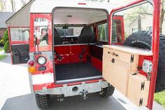 the back end of a red van with its doors open and two large tires parked in front of it