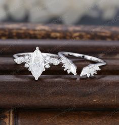 two silver rings with leaves on them sitting on top of a wooden table next to each other