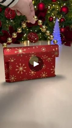 a hand reaching into a red box with gold decorations on it and a christmas tree in the background