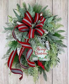 a christmas wreath with red and white ribbon hanging on a wooden wall next to a sign