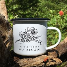 a white and black coffee mug sitting on top of a tree branch in front of some flowers