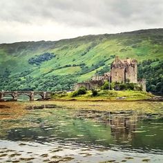 an old castle sitting on top of a lush green hillside next to a body of water