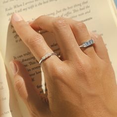 a woman's hand holding an open book with a diamond ring on her finger