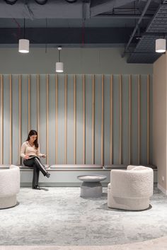 a woman is sitting on a bench in an office setting with round tables and stools