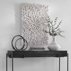 a white vase sitting on top of a black table next to a wall mounted art piece