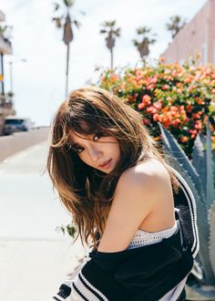 a woman leaning against a plant on the sidewalk