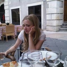 a woman sitting at a table with pizza and wine glasses in front of her, talking on the phone