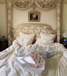 an unmade bed with white sheets and pink roses on the comforter next to it