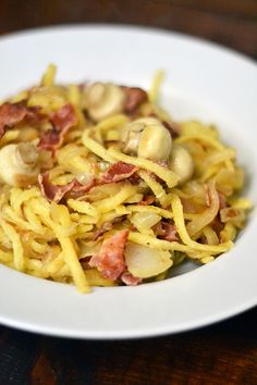 a white plate topped with pasta covered in bacon and mushrooms on top of a wooden table