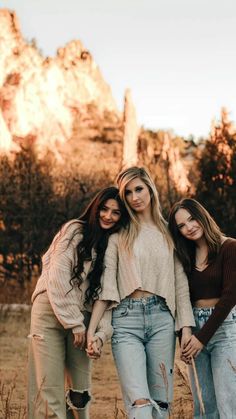 three young women standing next to each other in front of a mountain with trees and rocks