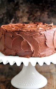 a chocolate cake sitting on top of a white cake plate next to a wooden table