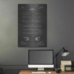 a desk with a computer, books and lamp on it in front of a gray wall