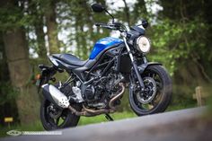 a blue and black motorcycle parked on the side of a road in front of trees