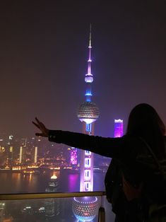 a woman standing on top of a tall building next to a body of water at night