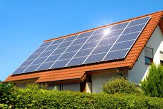 a house with a solar panel on the roof and some bushes in front of it