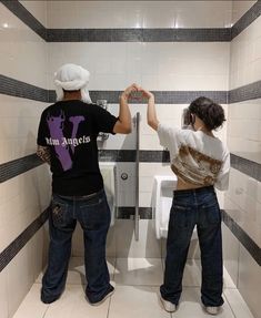 two people standing in a bathroom next to a urinal with their hands on the wall