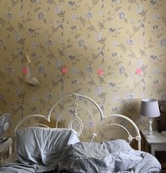 an unmade bed in front of a yellow wallpaper with pink flowers on it