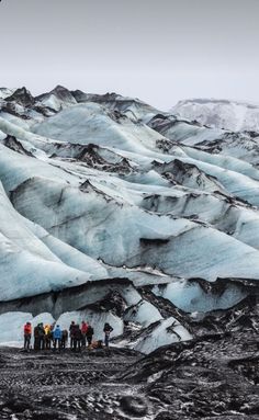 a group of people standing on top of a snow covered mountain next to a glacier