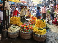 many people are shopping at an outdoor market with baskets full of flowers and other items