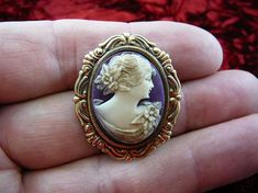 (Internal #CS45-9)  Excellent, new, hand stained natural pine resin, hand-molded (reproduced from the original shell cameo) small WAVY HAIRED WOMAN cameo pin/pendant in IVORY color with PURPLE color background color, mounted on repro Victorian brass, cameo itself is 3/4" across x 1" long. Clasp pin/pendant glued on back vertically. Excellent detail - beautiful, wavy hair caught with flowers/leaves at the back, a well defined flower at her shoulder, lovely draping of her gown, a pretty woman (rar Carved Oval Brooch As Gift, Carved Oval Brooches As Gift, Carved Oval Brooch For Gift, Beautiful Wavy Hair, Purple Color Background, Perfume Bottle Tattoo, Handmade Victorian Oval Brooches, Formal Cameo Pendant Brooch, Elegant Gold Cameo Brooch