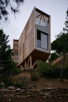 the house is made out of wood and sits on top of a hill surrounded by trees