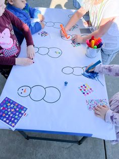 three children are sitting at a table with paper cut outs on it and colored pencils in front of them