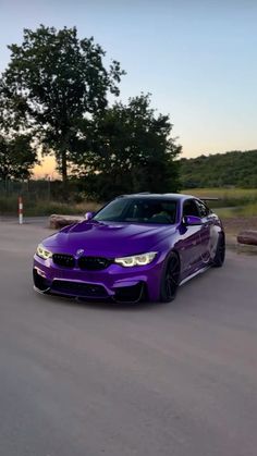 a purple car driving down a road next to some trees and bushes in the background