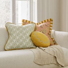 a white couch with pillows on it in front of a window