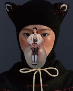 a woman wearing a cat hat and holding a bubble with her face in the shape of a doll