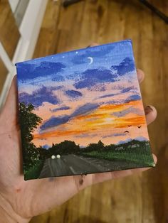 a person holding up a piece of art that looks like a sunset on the road